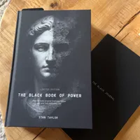 Customer-uploaded image. Click to see more details. The image represents: Two black books on a wooden surface - one titled "The Black Book of Power" by Stan Taylor with a classical statue face on the cover, and another smaller black book labeled "The Black Journal"
