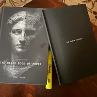 Customer-uploaded image. Click to see more details. The image represents: Two black books on a wooden surface - one titled "The Black Book of Power" by Stan Taylor with a classical statue image on the cover, and another titled "The Black Journal" alongside a yellow pen