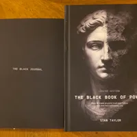 Customer-uploaded image. Click to see more details. The image represents: Two black books on a wooden surface - one titled "The Black Journal" and another titled "The Black Book of Power" by Stan Taylor with a classical statue face on the cover