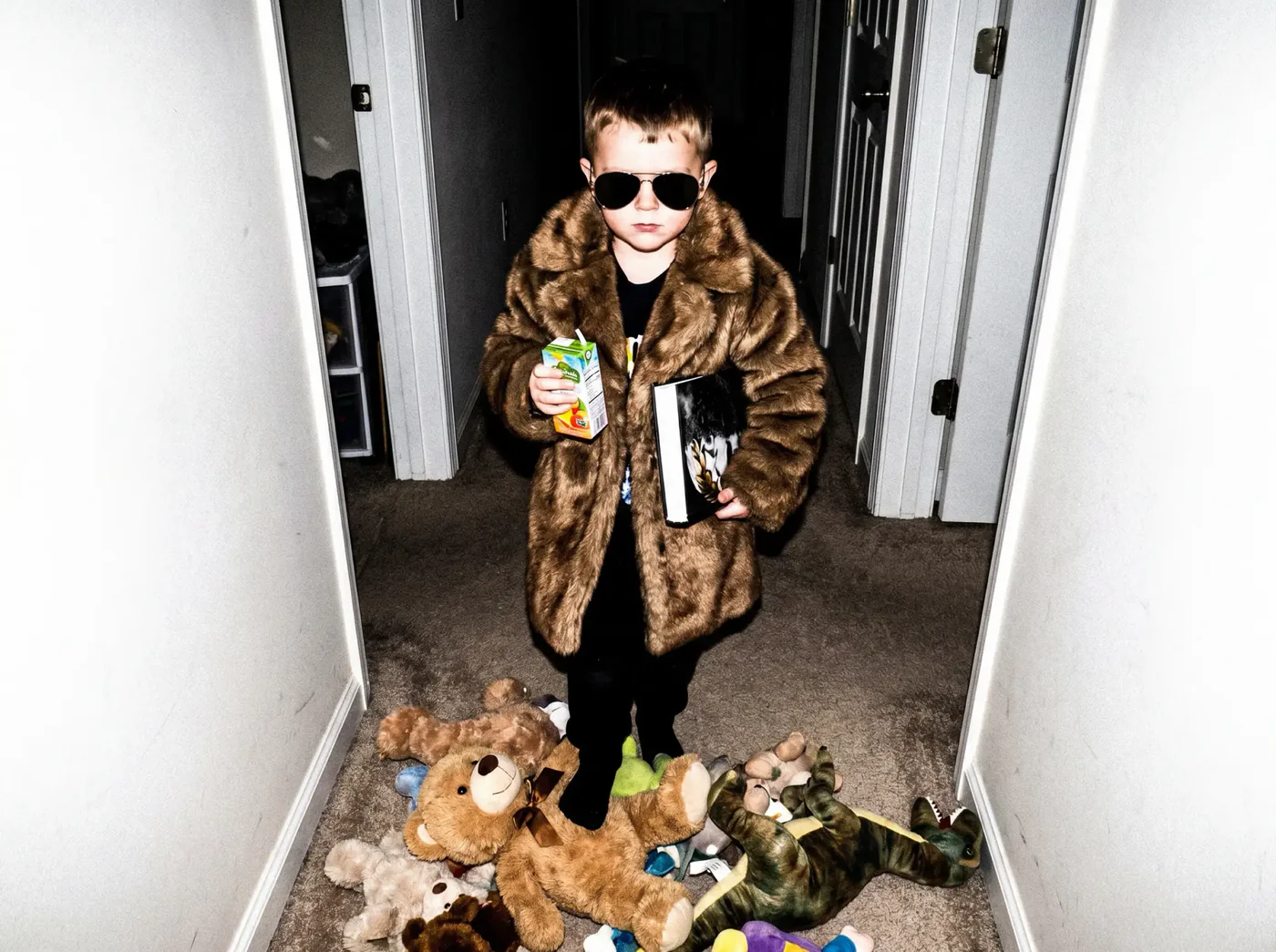 Child in fur coat and sunglasses amid scattered toys, drink in hand — The Little Dictator by Stan Taylor