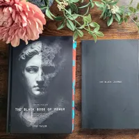 Customer-uploaded image. Click to see more details. The image represents: Two black books on a wooden surface with flowers - one titled "The Black Book of Power" by Stan Taylor with a classical statue image, and another titled "The Black Journal"